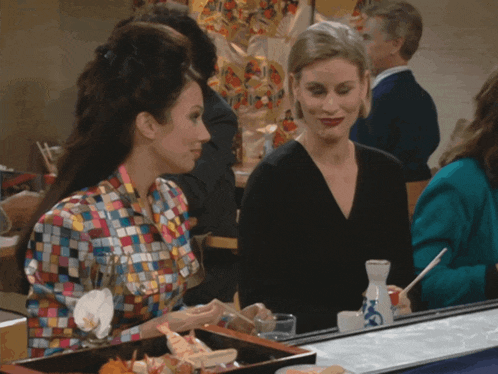 two women sit at a table with a bottle of sake on it