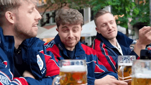 three men are sitting at a table with beer mugs in front of them .