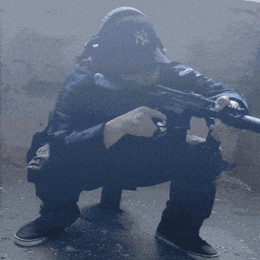 a man wearing a ny hat is kneeling down holding a gun