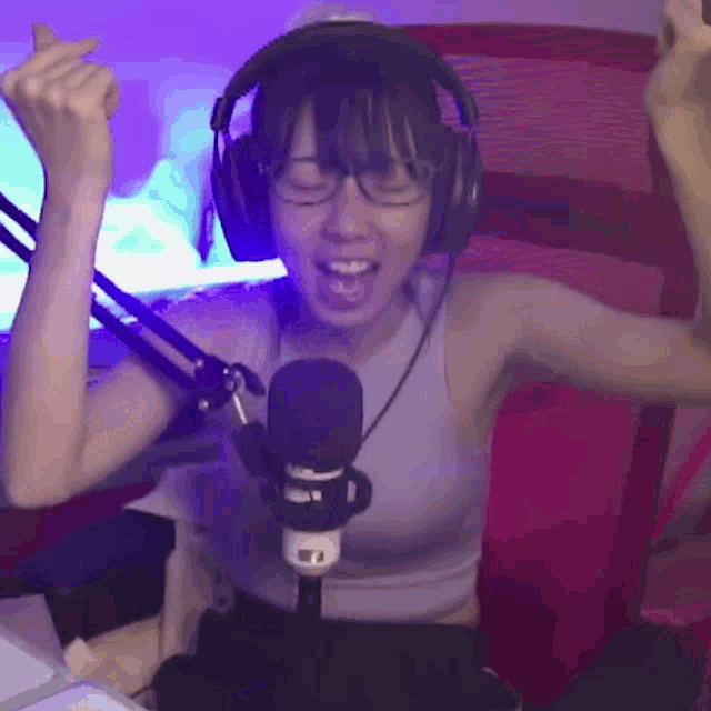 a woman wearing headphones and glasses is standing in front of a microphone .