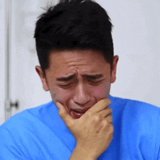 a man in a blue shirt is crying with his hand on his mouth .