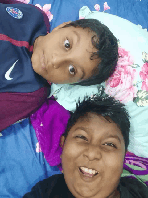 a boy wearing a nike shirt is laying on a bed next to another boy