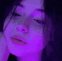 a close up of a girl 's face with a purple light behind her .