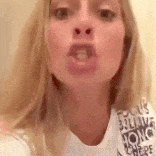 a close up of a woman 's face with her mouth open and a white shirt on .