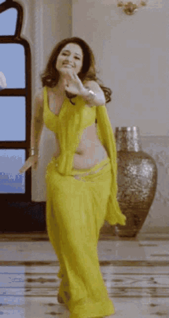 a woman in a yellow saree is dancing in a room