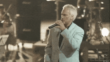 a man in a suit sings into a microphone in front of a marshall speaker