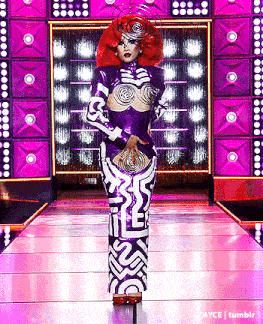 a drag queen with red hair is walking down a runway wearing a purple and white dress .