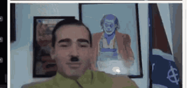 a man with a fake mustache is looking at the camera in front of a picture of a clown .