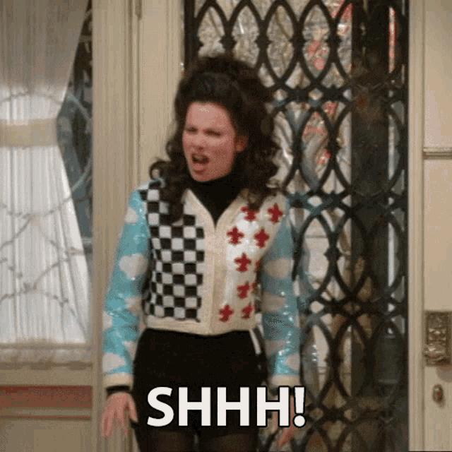 a woman is standing in front of a door wearing a checkered sweater and black shorts .