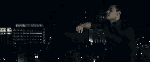 a man in a black shirt is standing in front of a city at night