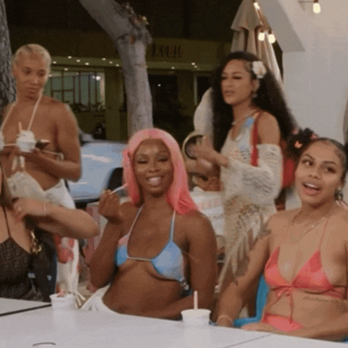 a group of women in bikinis are sitting at a table in front of a sign that says lulu