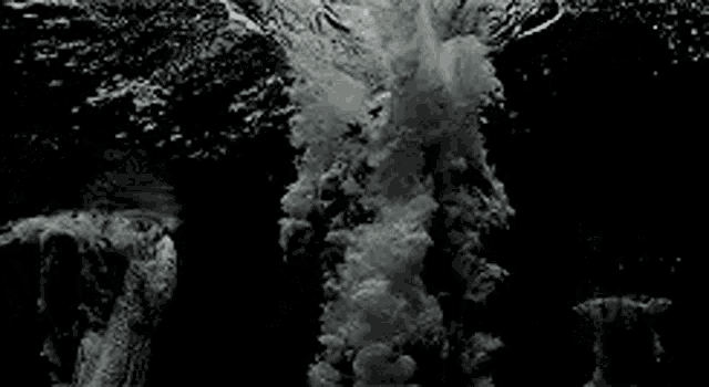 a black and white photo of a wave crashing on a rocky shore .
