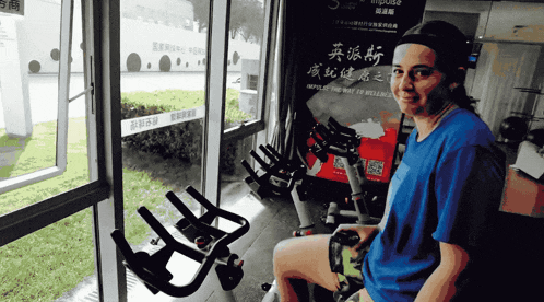 a woman sits on an exercise bike in front of a sign that says republic of wellness