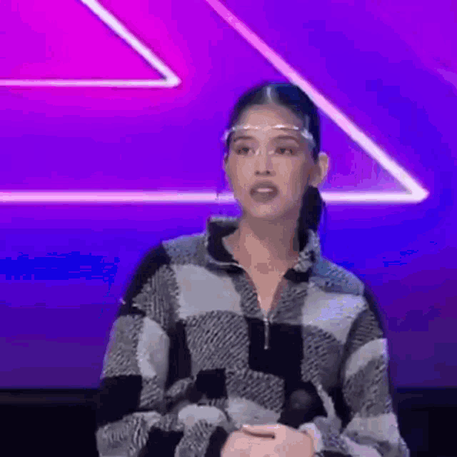 a woman wearing a face shield and a plaid jacket is standing in front of a microphone .