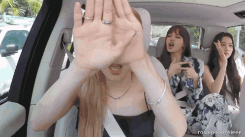 three women are sitting in a car and one of them is covering her face