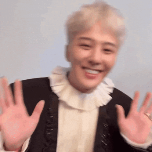 a blurry picture of a man wearing a white shirt and a black jacket smiling and waving .