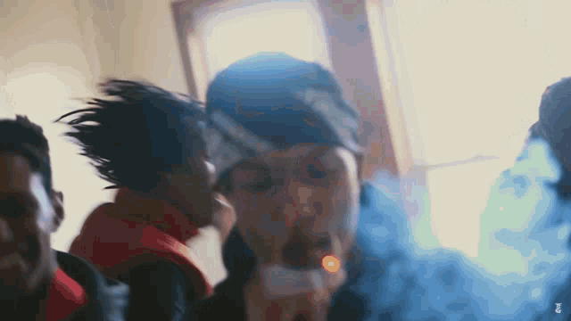 a man is smoking a cigarette in a room with other people .
