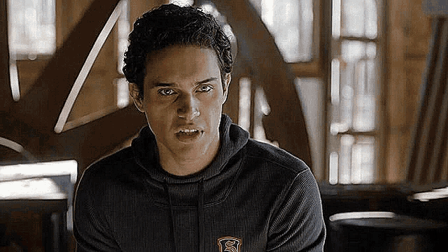 a young man in a black hoodie is sitting in a room looking at the camera .