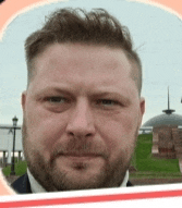 a man with a beard wearing a suit and tie looks at the camera