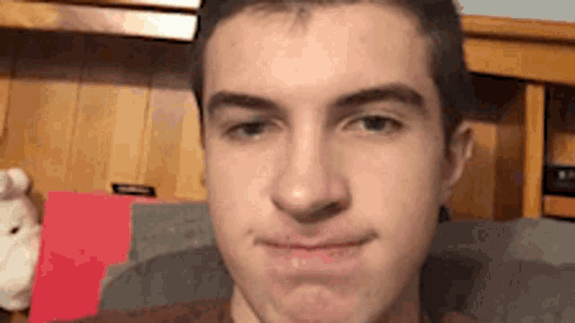 a young man is making a funny face while sitting on a couch in front of a stuffed animal .