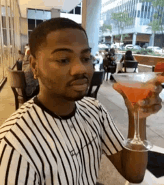 a man is holding a martini glass in his hand in a restaurant .