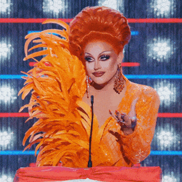 a drag queen wearing an orange feathered wig stands at a podium
