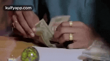 a person is holding a bunch of money in their hands on a table .