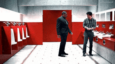 two men are standing next to each other in a public restroom .