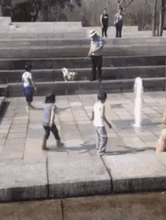 a group of children are playing in a fountain while a man holds a dog .