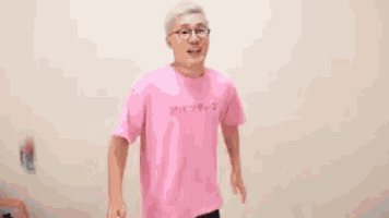 a man wearing glasses and a pink shirt is standing in front of chinese writing