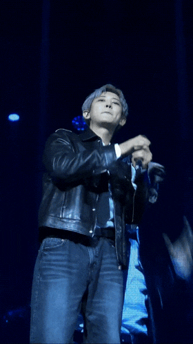 a man in a leather jacket and tie is holding a microphone on a stage