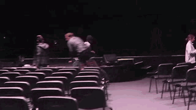a group of people are standing in a dark room with rows of chairs