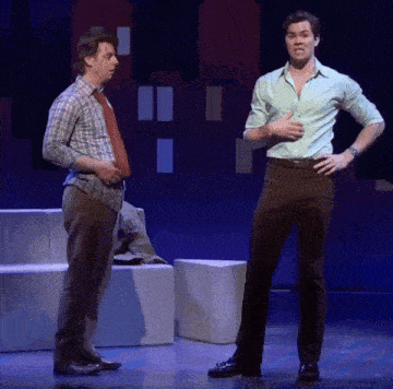 two men standing on a stage with their hands on their hips talking to each other