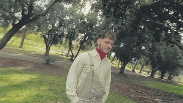 a man wearing overalls and a white shirt is walking through a park