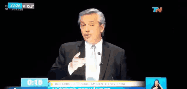 a man in a suit is giving a speech on a television screen