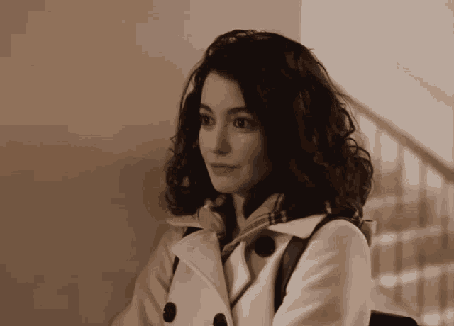 a woman with curly hair wearing a white coat and scarf