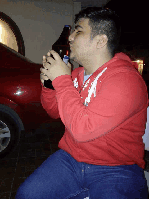 a man in a red hoodie drinks from a bottle