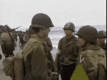 a group of soldiers are standing on a beach near the ocean .