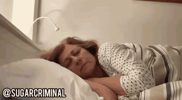 a woman is sleeping in a bed with the words sugarcriminal written on the bottom of the screen .
