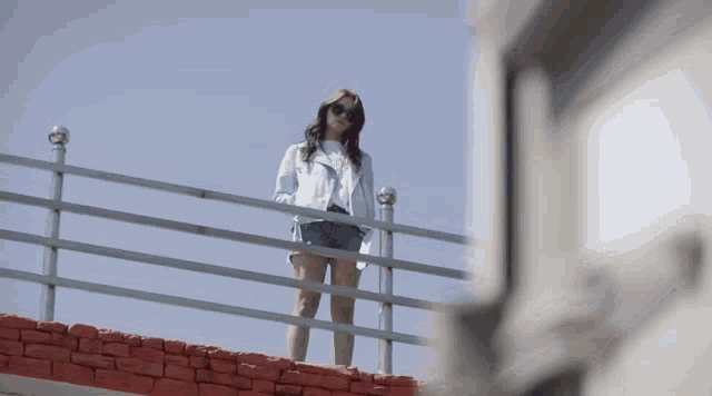 a woman wearing shorts and sunglasses stands on a fence