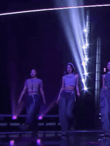 a group of women are dancing on a stage in front of purple lights