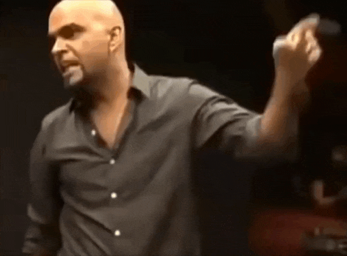 a bald man in a black shirt is standing in front of a microphone .