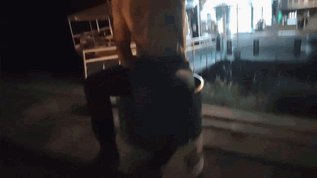 a person standing in front of a building at night with a bucket in front of them