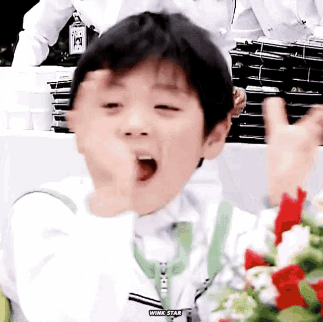 a young boy is making a funny face while sitting in front of a table with flowers .