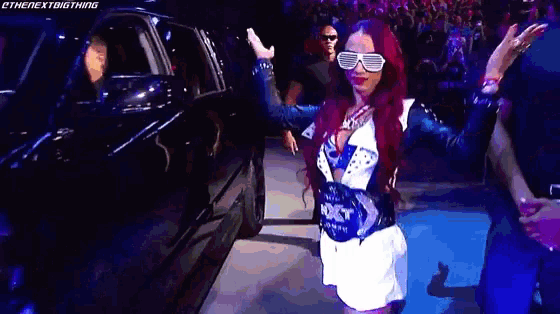 a woman wearing sunglasses and a belt is standing in front of a black car .