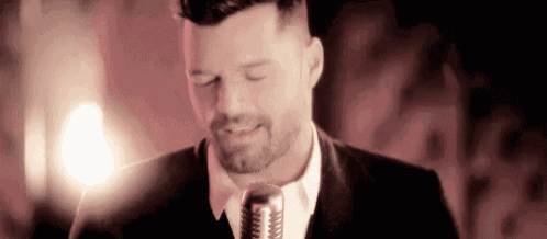 a man in a suit is singing into a microphone in a dark room .