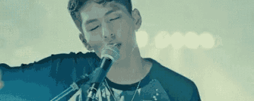 a young man is singing into a microphone while wearing a black shirt .