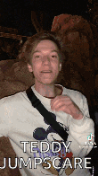 a young man wearing a mickey mouse sweater is standing in front of a rock .