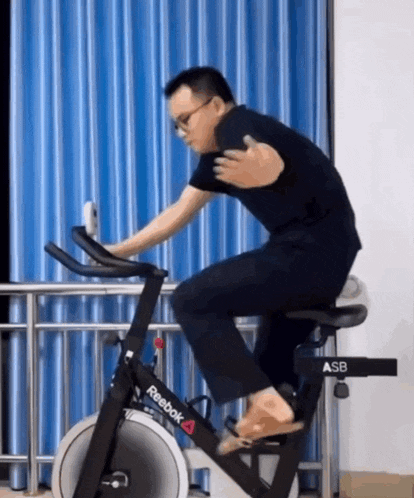 a man is riding a reebok exercise bike in front of a blue curtain