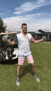 a man in an american flag shirt is standing in front of a golf cart holding a can of soda .
